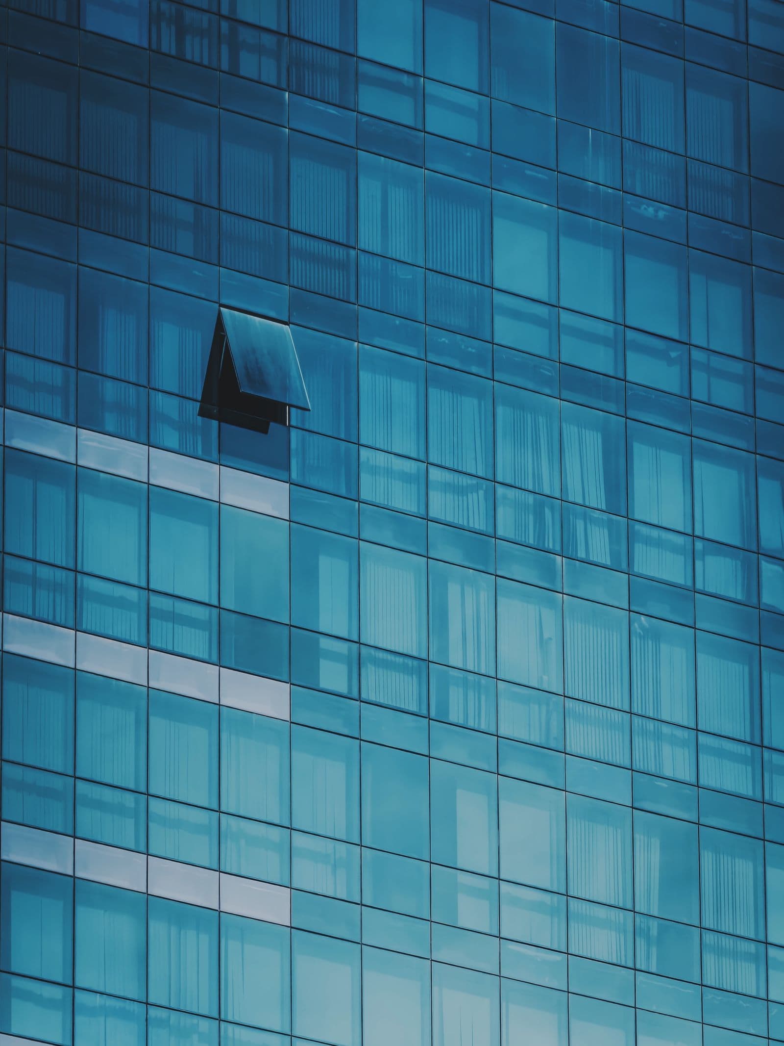 A teal glass curtain wall with a single window propped open